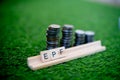 Wooden blocks spelling EPF with a stack of coins growing in size set on grass