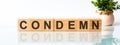 Wooden Blocks with the text: condemn. The text is written in black letters and is reflected in the mirror surface of the table