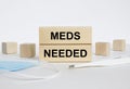 Wooden blocks with text Meds Needed with mask and thermometer