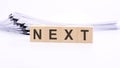 wooden blocks with text NEXT on white table, stack white paper on background Royalty Free Stock Photo