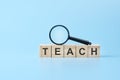 wooden blocks with the text: teach with magnifying glass. business concept