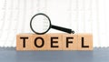 On wooden blocks under a magnifying glass text: TOEFL. Educational concept. TOEFL - words from wooden blocks with letters, Test of