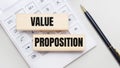 Wooden blocks with the VALUE PROPOSITION Iie on a light background on a white calculator. Nearby is a black handle. Business