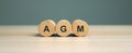 Wooden blocks with the word AGM - Annual general meeting. Mandatory yearly gathering of a company\'s interested shareholders.