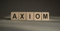 A wooden blocks with the word AXIOM written on it on a gray background