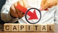 Wooden blocks with the word Capital and arrow down in the hands of a businessman. The concept of the fall in the level of Royalty Free Stock Photo
