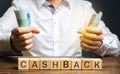 Wooden blocks with the word Cashback and money in the hands of a businessman. Bonus program to attract customers and increase