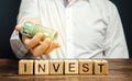 Wooden blocks with the word Invest and money in the hands of a businessman. Concept of investing in a business project. Economics Royalty Free Stock Photo