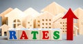 Wooden blocks with the word rates, up arrow and miniature houses. The concept of high interest rates on mortgages. Real estate.