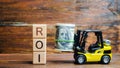 Wooden blocks with the word ROI and money with forklift. Ratio between the net profit and cost of investment resulting from an Royalty Free Stock Photo