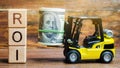 Wooden blocks with the word ROI and money with forklift. Ratio between the net profit and cost of investment resulting from an Royalty Free Stock Photo