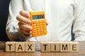 Wooden blocks with the word Tax time and taxpayer with a calculator. The concept of paying the tax rate. Taxation / burden. Pay Royalty Free Stock Photo