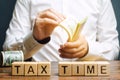 Wooden blocks with the word Tax time and taxpayer with a money. Property / income annual taxes. The concept of paying the tax rate