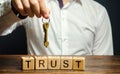 Wooden blocks with the word Trust and keys in the hands of a businessman. Entrust apartment, car, property and real estate. Credit Royalty Free Stock Photo