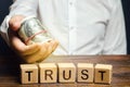 Wooden blocks with the word Trust and money in the hands of a businessman. Trust relationships between business partners, friends Royalty Free Stock Photo