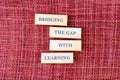 Wooden blocks with the words BRIDGING THE GAP WITH LEARNING are aligned vertically. The textured, woven surface provides a vibrant Royalty Free Stock Photo