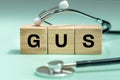 Wooden blocks with the words GUS, urogenital system, medical stethoscope, health concept, regular examinations