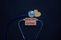 Wooden blocks with words `healthy eating` and stethoscope on black background. Wooden heart. Medical and lifestyle concept