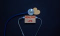 Wooden blocks with words `healthy life` and stethoscope on black background. Wooden heart. Medical and lifestyle concept