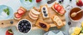 A wooden board of breakfast crackers topped with spreads and fresh toppings.