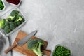 Wooden board, broccoli, knife and containers with fresh products on light gray marble table, flat lay with space for text. Food