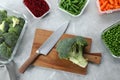 Wooden board with broccoli, knife and containers with products on light gray marble table, flat lay. Food storage
