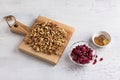 Wooden board with chopped walnuts, bowls with dried cranberries and spices on light gray textured background, top view.