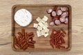 A wooden board with delicacies on which pieces of meat and various types of cheese lie, on the kitchen counter, top view. Royalty Free Stock Photo
