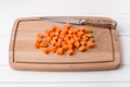 Wooden board with diced carrots on white wooden background