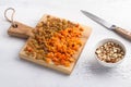 A wooden board with dried fruits - raisins and chopped dried apricots, a bowl with chopped hazelnuts and a knife on a light gray Royalty Free Stock Photo