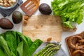 Wooden board and fresh vegetables around. Asparagus on napkin, avocados, peanuts in bowl, pretzel, romano salad and