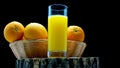 On a wooden board Freshly squeezed orange juice in a glass on a black background. Oranges in a basket with fresh yellow lemonade