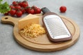 Wooden board with grater, cheese and vegetables on grey table Royalty Free Stock Photo