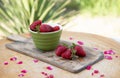 Wooden board with green bowl strawberries lying on table with roses petals outdoor.