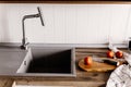 wooden board with knife, tomatoes, towel, spices on modern kitchen countertop near granite sink and steel faucet with water. coo Royalty Free Stock Photo