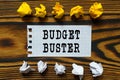 On a wooden board lie crumpled leaves of paper and a sheet from a notebook on which it is written - BUDGET BUSTER