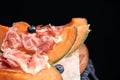 Wooden board with melon, prosciutto and blueberries on table against black background Royalty Free Stock Photo