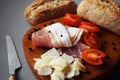 Wooden board with slices of bacon, parmesan, cherry tomatoes, black peppercorns next to bread and knife Royalty Free Stock Photo