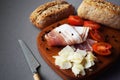 Wooden board with slices of bacon, parmesan, cherry tomatoes, black peppercorns next to bread and knife Royalty Free Stock Photo