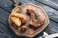 Wooden board with tasty grilled steak, potato and mushrooms on table Royalty Free Stock Photo