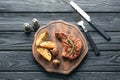 Wooden board with tasty grilled steak, potato and mushrooms on table Royalty Free Stock Photo