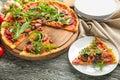 Wooden board with tasty pizza and plate with slice on table Royalty Free Stock Photo