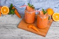A wooden board with two mason jars with carrot smoothie, basil, oranges and leaves of mint on a light background. Royalty Free Stock Photo