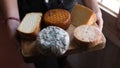 Wooden board with a wide variety of cheeses of different types, held by one person. Blue cheese, smoked cheese