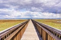 Wooden boardwalk going over the marshes of south San Francisco bay area; electricity towers and lines visible against the cloudy Royalty Free Stock Photo
