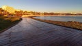 Wooden Boardwalk at sunrise leading to holiday resort lit by morning sun, beach and bay with hotels, restaurants, cafes and palm Royalty Free Stock Photo