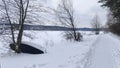 A wooden boat is leaning sideways against a tree on the shore of a frozen lake near a beaten path. After the snowfall, everything Royalty Free Stock Photo