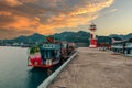 Wooden boat moored at a dock in a tranquil harbor near a historic lighthouse in Thailand.