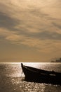 A wooden boat near the seashore in the orange rays of sunset against the background of clouds and sky haze