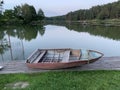 Wooden boat on the pier on the background of the lake. Fishing boat on the shore of a forest reservoir. The boat is tied off the